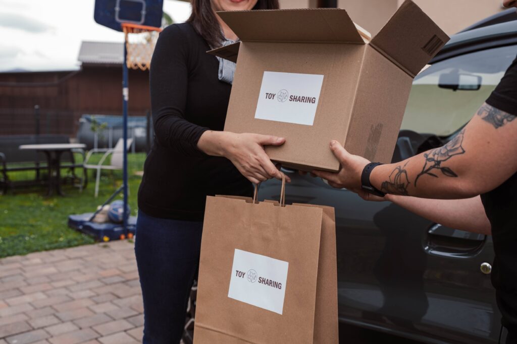 Person handing over a ToySharing Montessori toy box and bag next to a car.