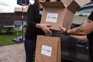 Person handing over a ToySharing Montessori toy box and bag next to a car.